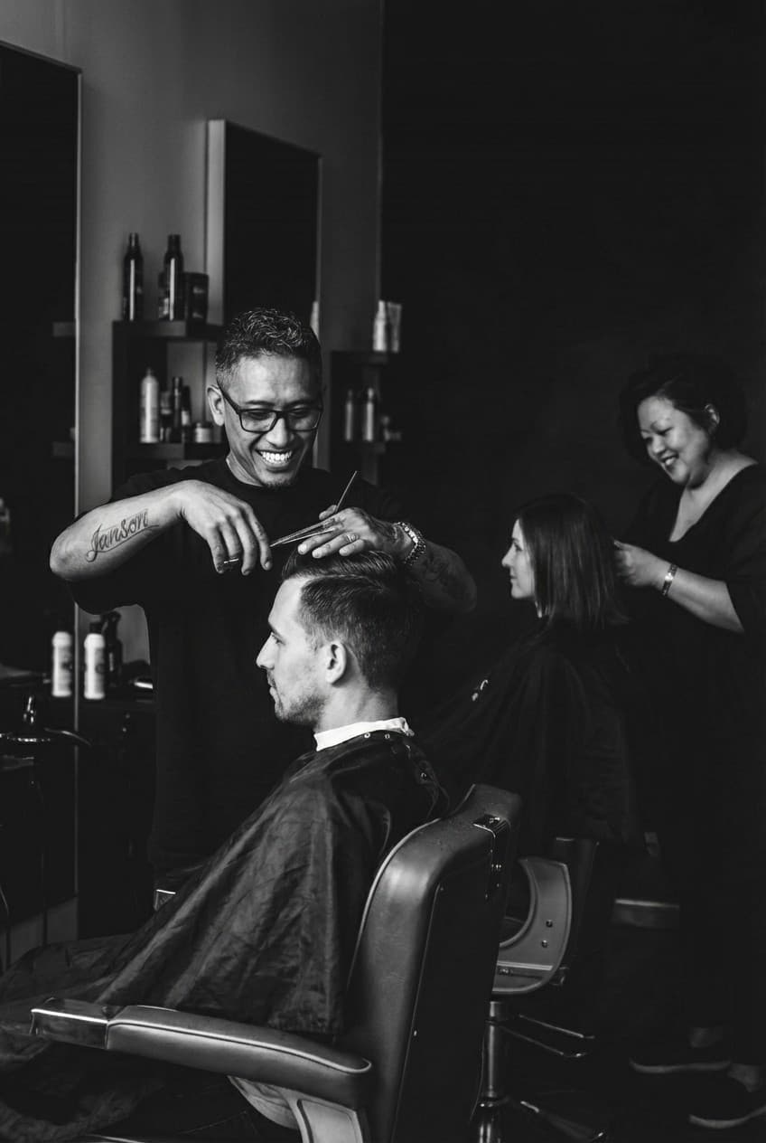 Marvin cutting a client’s hair, with Melissa working in the background